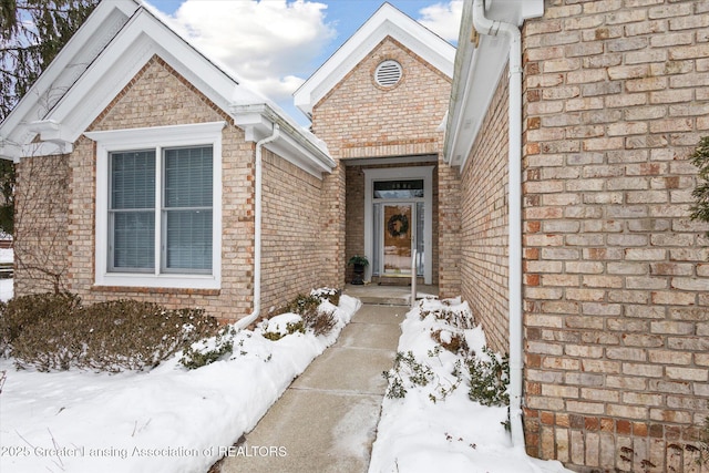 snow covered property entrance featuring brick siding