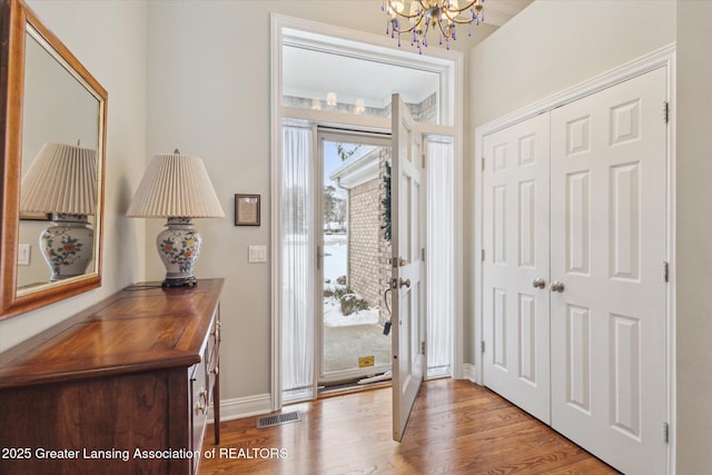 entryway with an inviting chandelier, wood finished floors, visible vents, and baseboards