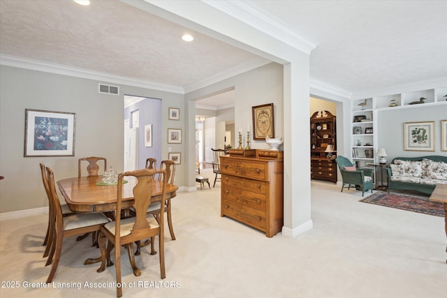 dining room with visible vents, baseboards, built in features, ornamental molding, and light carpet