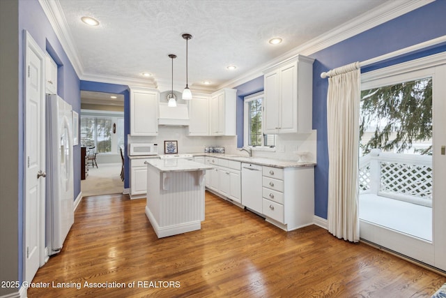 kitchen featuring ornamental molding, a sink, a center island, white appliances, and white cabinets