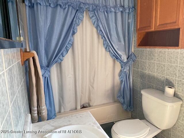 bathroom with shower / bathtub combination with curtain, toilet, and tile walls