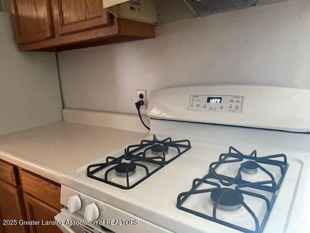 kitchen featuring white gas range, brown cabinetry, and light countertops