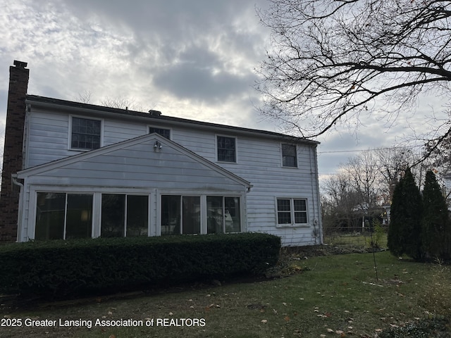 rear view of house featuring a lawn, a sunroom, and a chimney