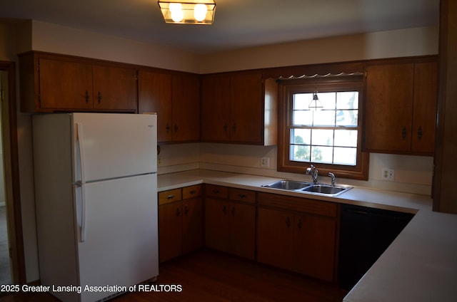 kitchen with brown cabinetry, freestanding refrigerator, a sink, light countertops, and black dishwasher