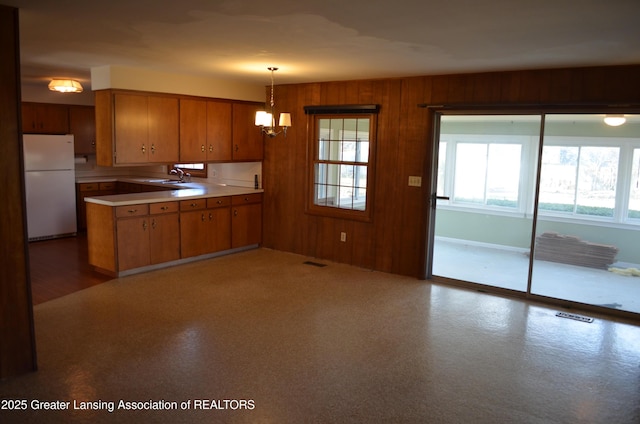 kitchen with brown cabinetry, wood walls, light countertops, and freestanding refrigerator