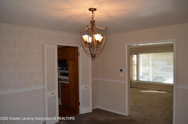 unfurnished dining area featuring baseboards, a chandelier, dark carpet, and wallpapered walls