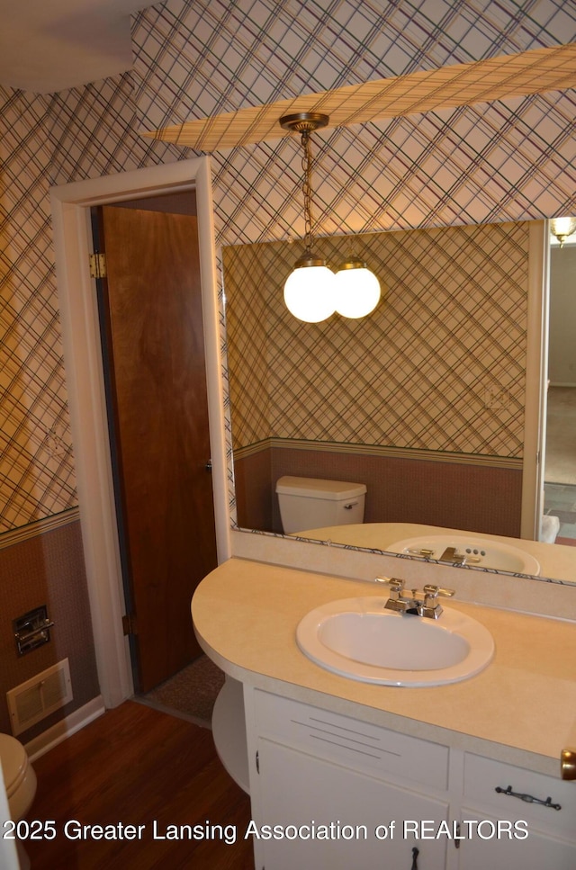 bathroom with wallpapered walls, toilet, vanity, and visible vents