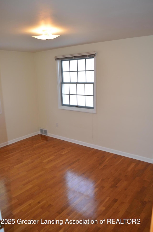 unfurnished room with wood finished floors, visible vents, and baseboards