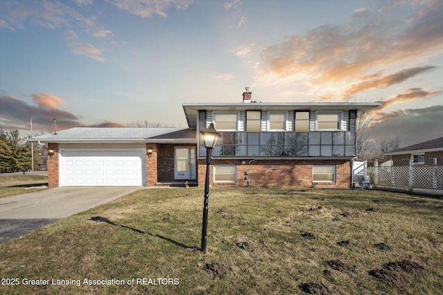 split level home with brick siding, concrete driveway, a front yard, a chimney, and an attached garage