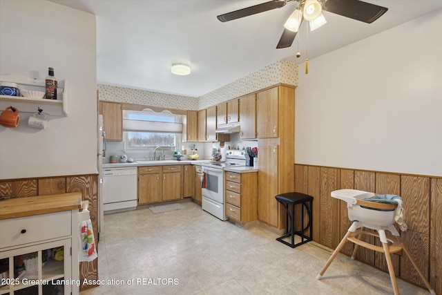 kitchen featuring under cabinet range hood, a sink, white appliances, wainscoting, and light countertops