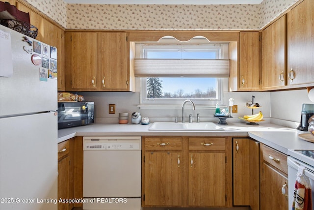 kitchen with brown cabinetry, white appliances, light countertops, and a sink