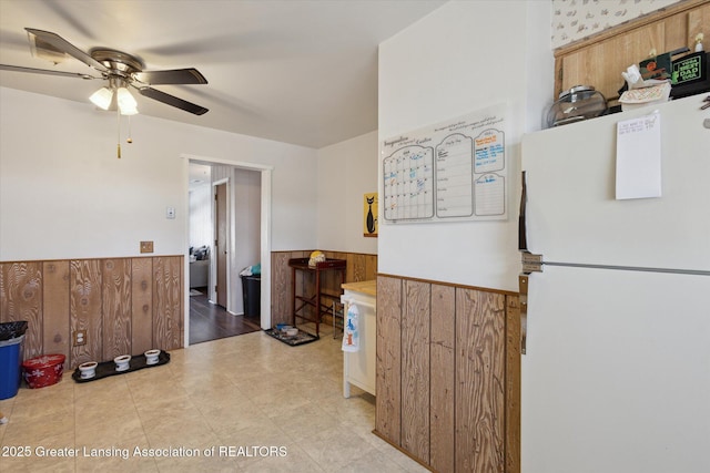 kitchen with a ceiling fan, wooden walls, wainscoting, and freestanding refrigerator