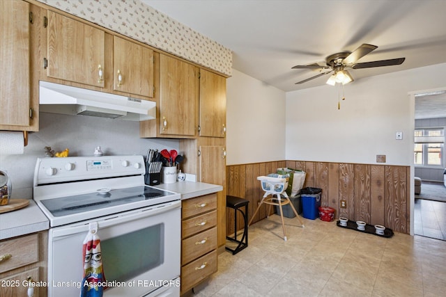 kitchen featuring wooden walls, a wainscoted wall, light countertops, electric stove, and under cabinet range hood