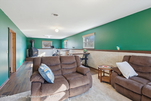 living area with visible vents, a wood stove, a wainscoted wall, and wood finished floors