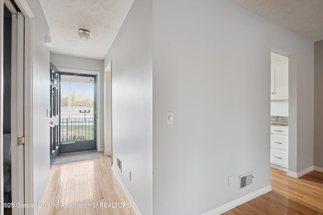 corridor with light wood-style floors, baseboards, a textured ceiling, and visible vents