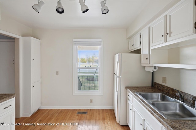 kitchen featuring visible vents, light wood-style flooring, a sink, white cabinets, and baseboards