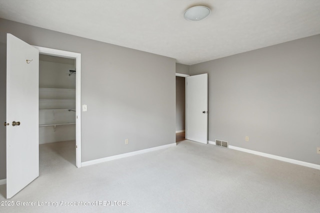 unfurnished bedroom with a spacious closet, visible vents, baseboards, carpet, and a closet