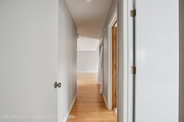 hall featuring light wood-style flooring, baseboards, and a textured ceiling