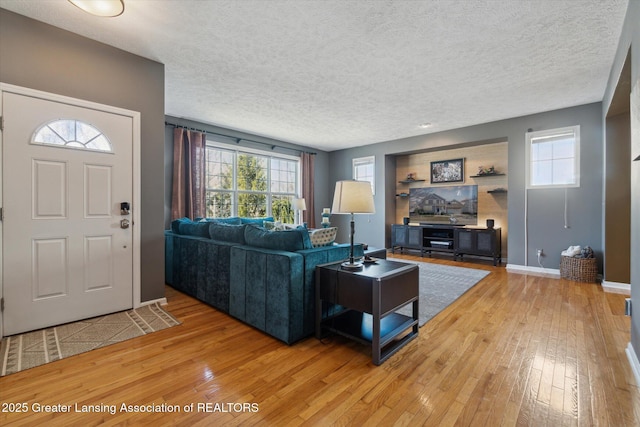 living area featuring light wood finished floors, a textured ceiling, and baseboards