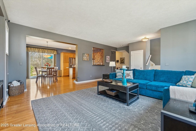 living area featuring stairs, baseboards, light wood finished floors, and a textured ceiling