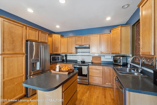 kitchen with under cabinet range hood, dark countertops, appliances with stainless steel finishes, and a sink