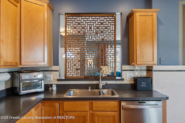 kitchen with stainless steel dishwasher, dark countertops, tasteful backsplash, and a sink