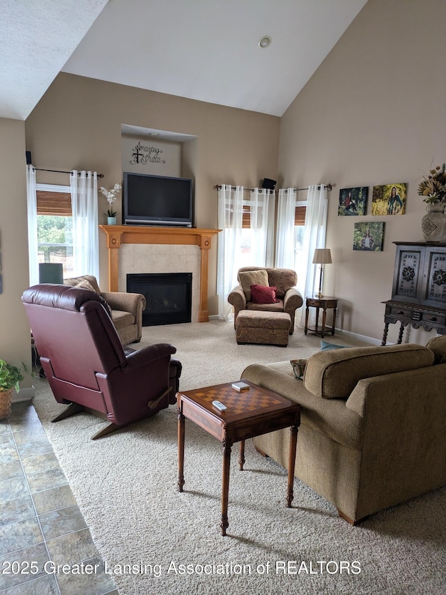 carpeted living area featuring a tiled fireplace and high vaulted ceiling