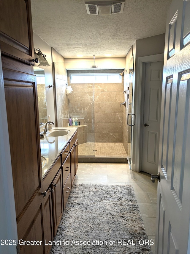 bathroom with visible vents, double vanity, a sink, a shower stall, and a textured ceiling