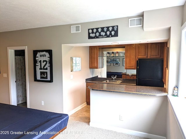 kitchen with a sink, visible vents, brown cabinetry, and freestanding refrigerator