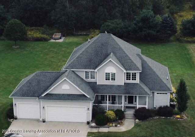 view of front facade with covered porch, a shingled roof, a front lawn, concrete driveway, and a garage