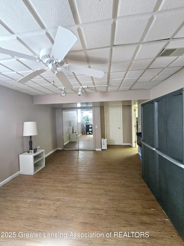 basement with wood finished floors, visible vents, baseboards, ceiling fan, and a paneled ceiling