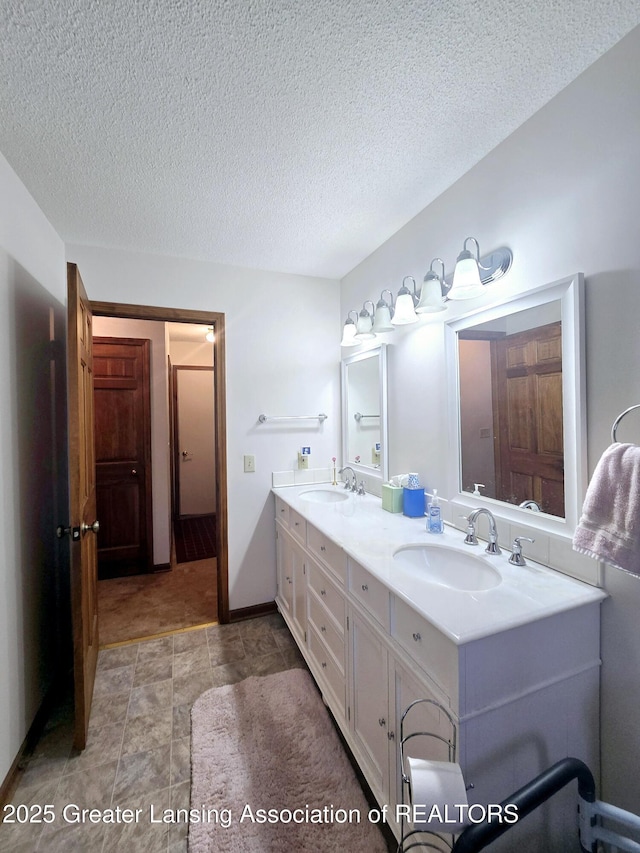 bathroom with a sink, baseboards, a textured ceiling, and double vanity