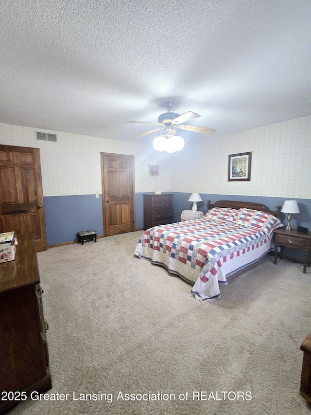 bedroom with visible vents, carpet floors, a textured ceiling, and wallpapered walls