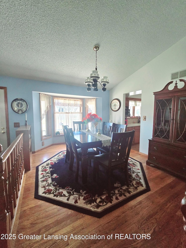 dining room with an inviting chandelier, wood finished floors, visible vents, and lofted ceiling