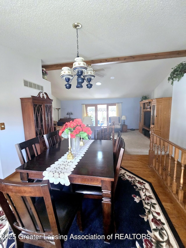 carpeted dining room featuring lofted ceiling with beams, visible vents, a textured ceiling, and a chandelier