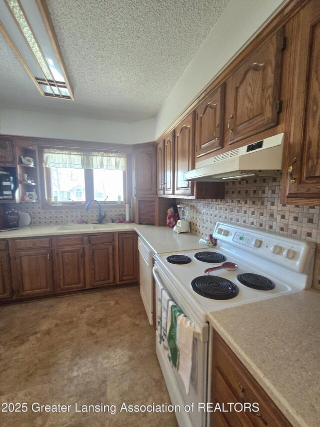 kitchen with a sink, under cabinet range hood, backsplash, white appliances, and light countertops