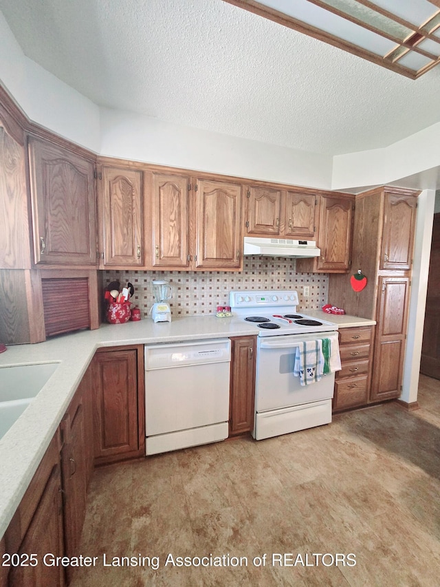 kitchen with under cabinet range hood, tasteful backsplash, white appliances, brown cabinetry, and light countertops