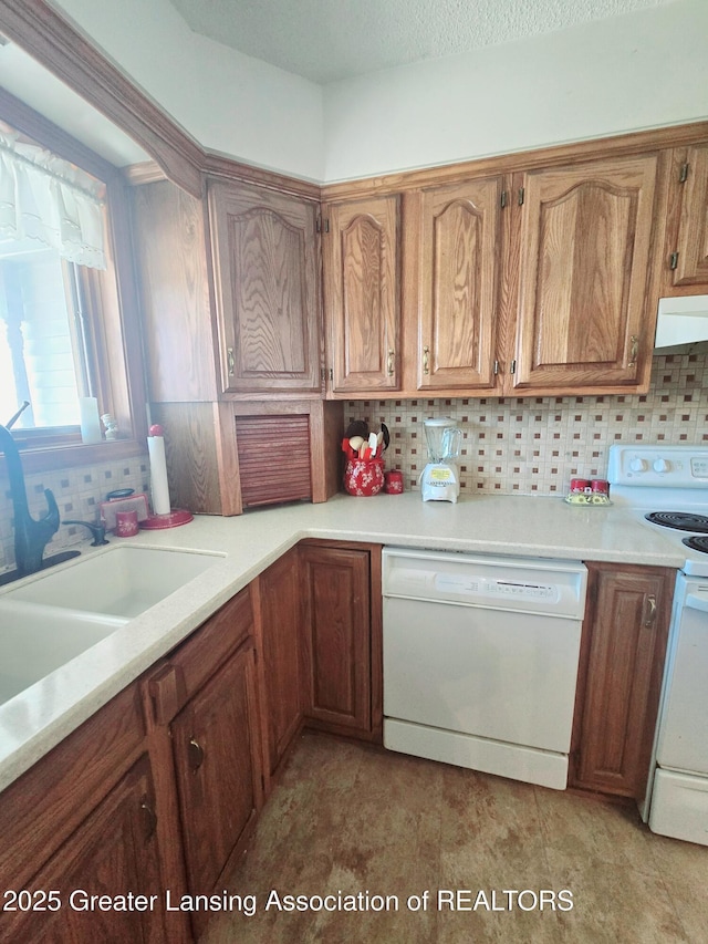 kitchen featuring brown cabinets, under cabinet range hood, backsplash, white appliances, and light countertops