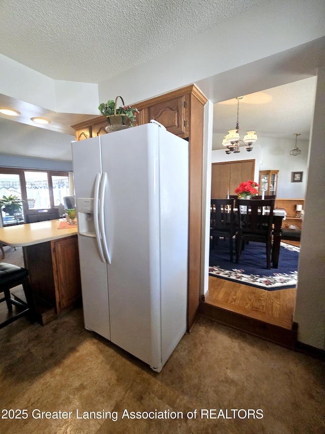 kitchen featuring an inviting chandelier, light countertops, white refrigerator with ice dispenser, a textured ceiling, and brown cabinets