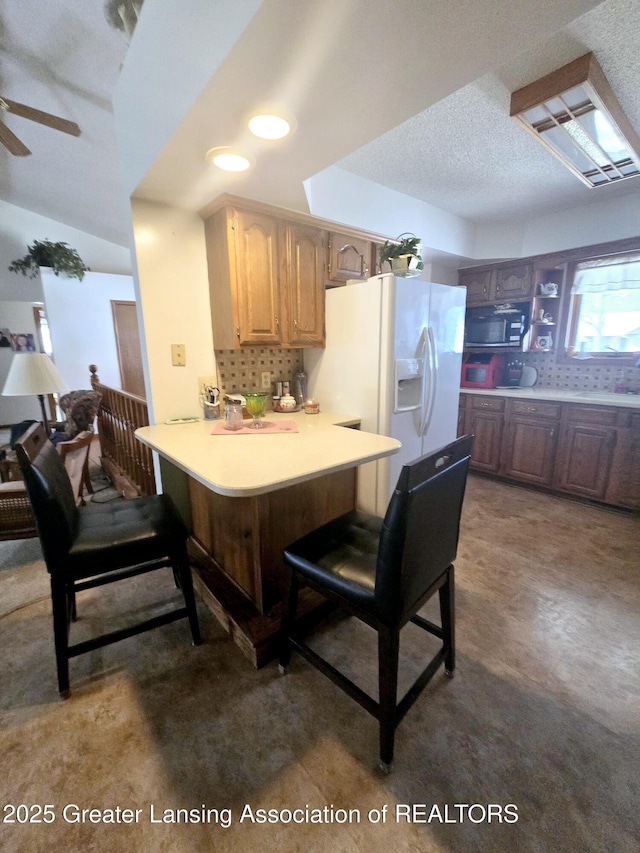 kitchen featuring a breakfast bar, backsplash, white refrigerator with ice dispenser, a peninsula, and light countertops