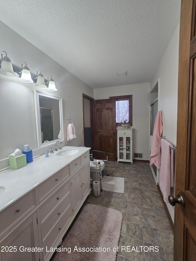 bathroom with vanity, an enclosed shower, visible vents, and a textured ceiling