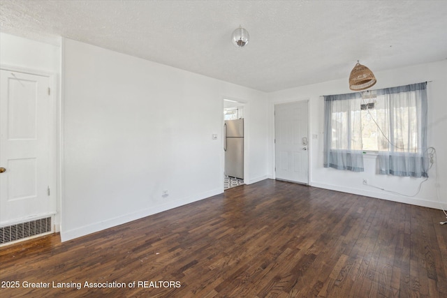 spare room with dark wood-style floors, visible vents, a textured ceiling, and baseboards