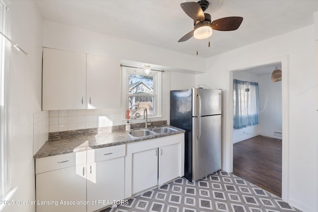 kitchen featuring dark countertops, backsplash, freestanding refrigerator, a ceiling fan, and a sink