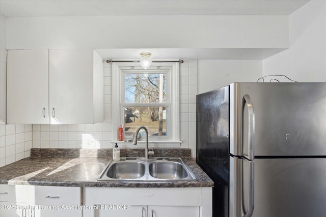 kitchen with a sink, dark countertops, white cabinetry, freestanding refrigerator, and decorative backsplash