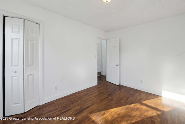 unfurnished bedroom featuring a closet, a textured ceiling, baseboards, and wood finished floors