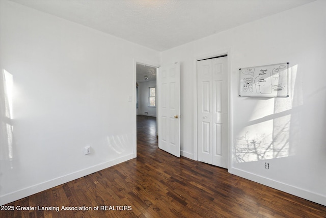 unfurnished bedroom featuring dark wood-type flooring, baseboards, and a closet