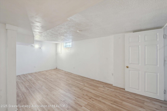 basement featuring baseboards, light wood-style floors, and a textured ceiling