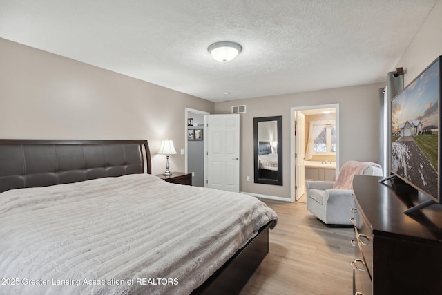 bedroom featuring visible vents, baseboards, light wood-type flooring, ensuite bathroom, and a textured ceiling