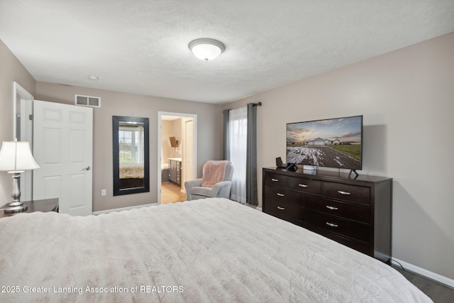 bedroom featuring ensuite bath, visible vents, a textured ceiling, and baseboards