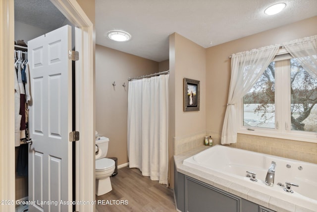 full bathroom featuring a spacious closet, toilet, a garden tub, wood finished floors, and a textured ceiling